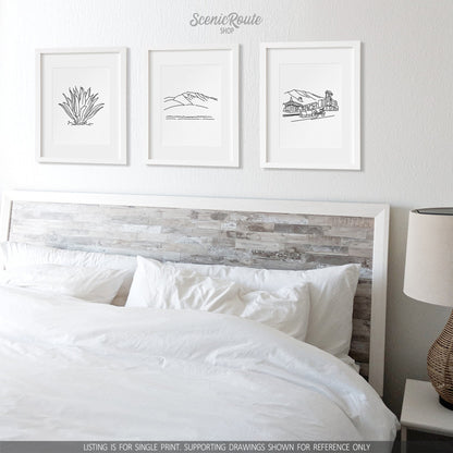A group of three framed drawings on a white wall above a bed. The line art drawings include an Agave Cactus, Humphreys Peak, and the Flagstaff Skyline
