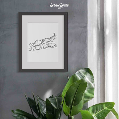 A framed line art drawing of The Flatiron Mountains hung on the wall above a plant near a window