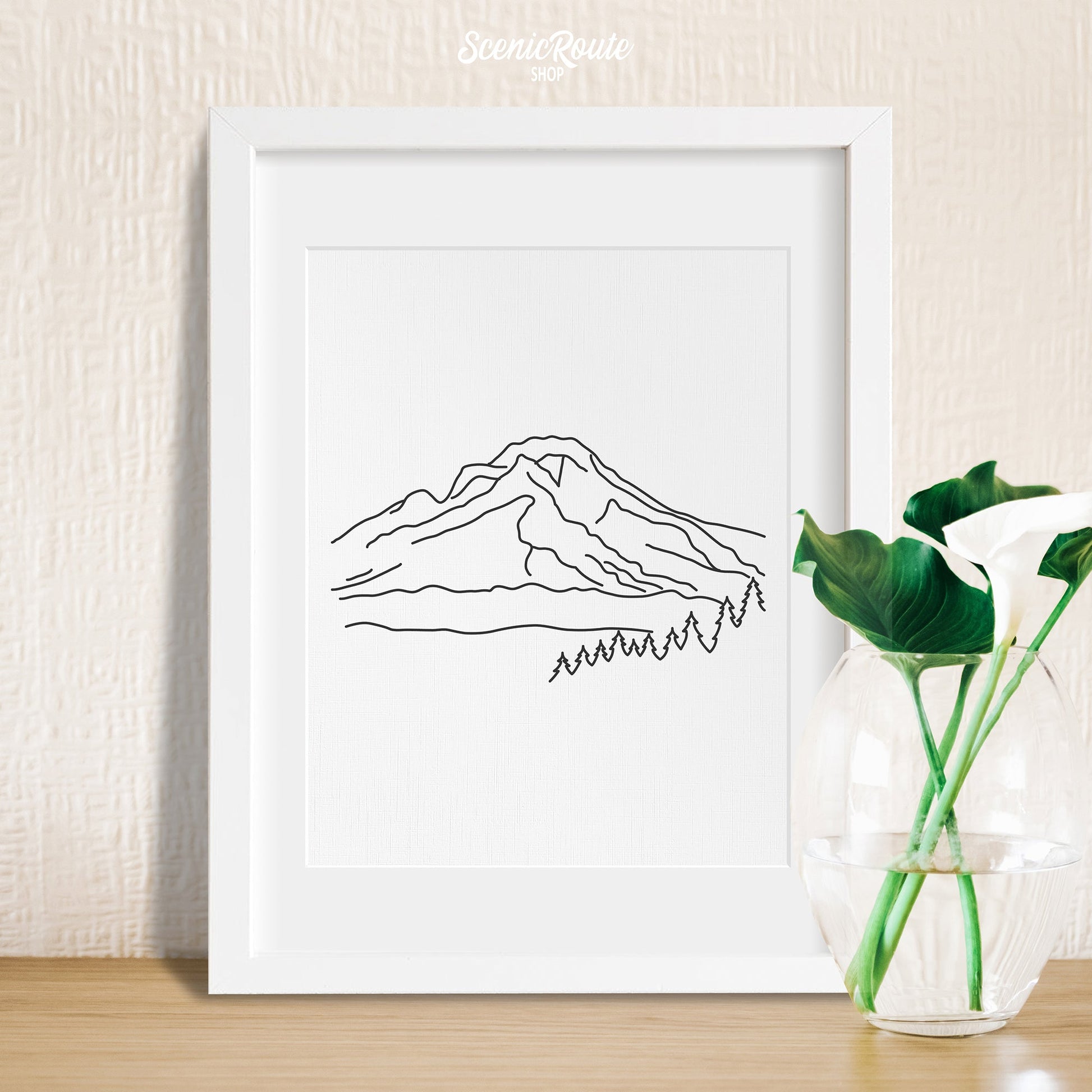 A framed line art drawing of Mount Hood with a vase