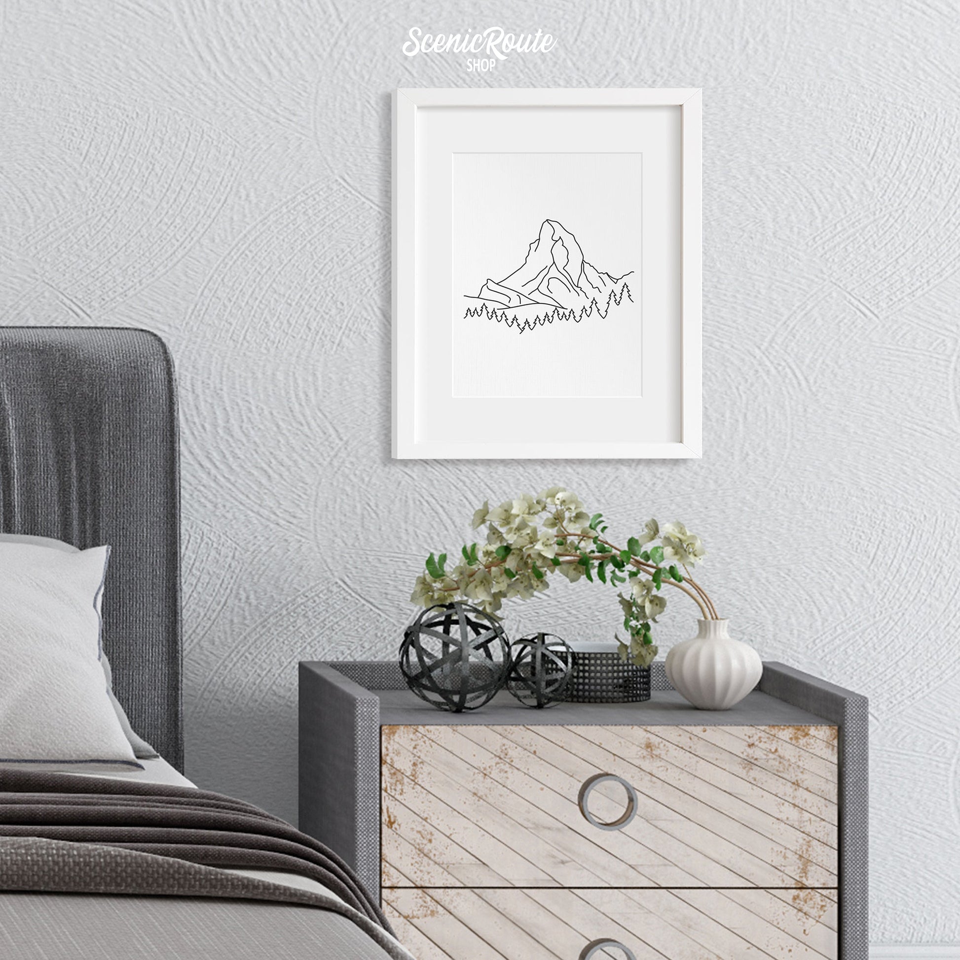 A framed line art drawing of The Matterhorn above a nightstand next to a bed