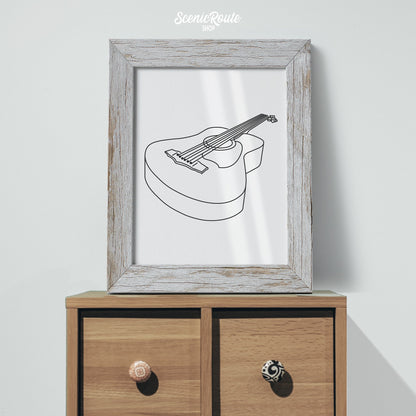 A framed line art drawing of a Guitar on a small cabinet