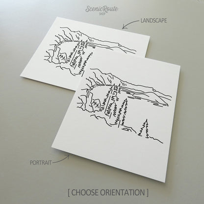 Two line art drawings of Crater Lake National Park on white linen paper with a gray background.  The pieces are shown in portrait and landscape orientation for the available art print options.