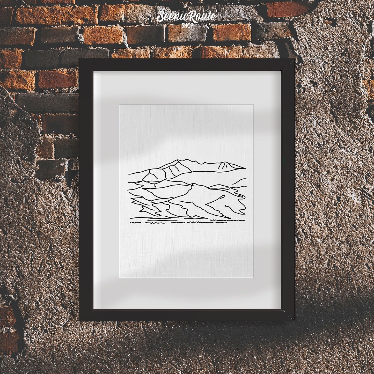 A framed line art drawing of Great Sand Dunes National Park on a rough brick wall
