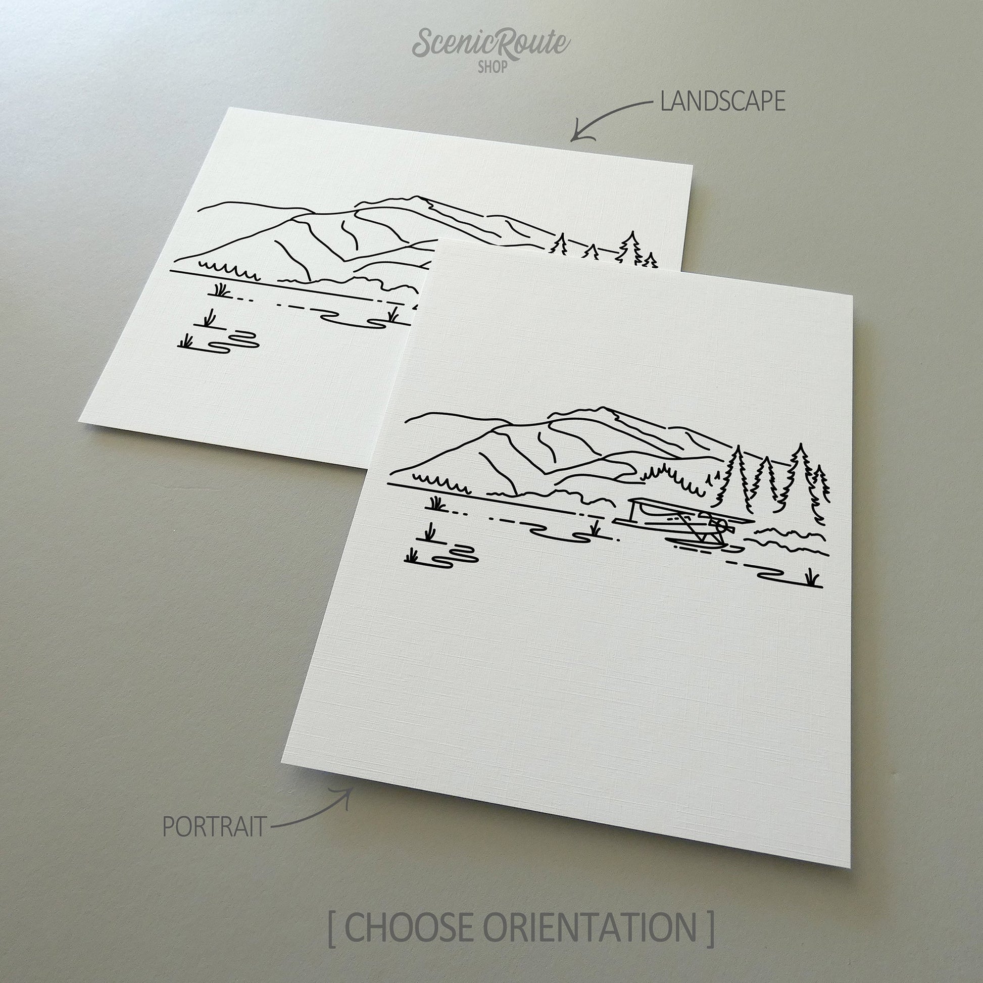 Two line art drawings of Lake Clark National Park on white linen paper with a gray background.  The pieces are shown in portrait and landscape orientation for the available art print options.