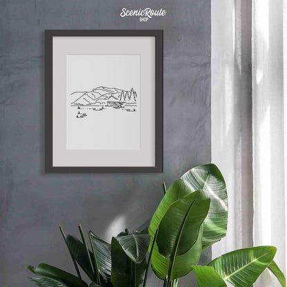 A framed line art drawing of Lake Clark National Park on a gray wall above a tropical plant