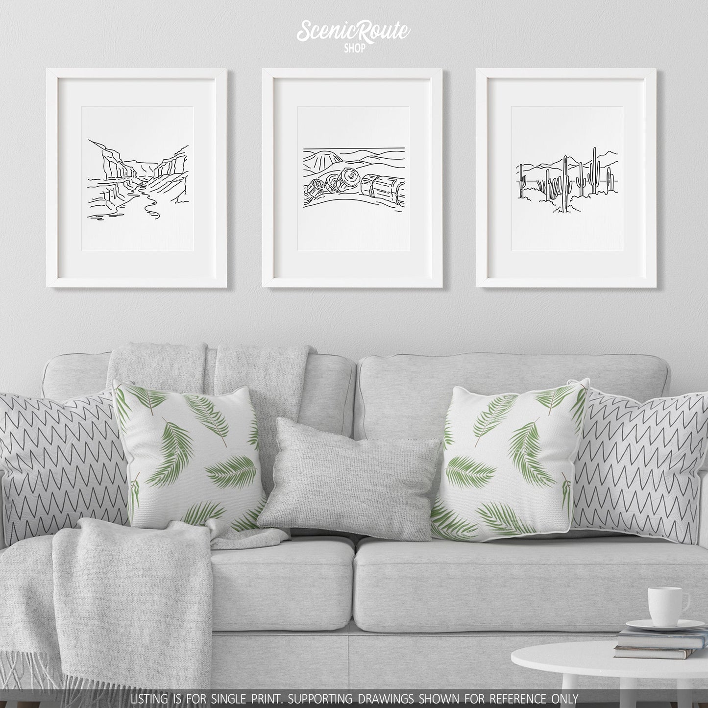 A group of three framed drawings on a white wall hanging above a couch with pillows and a blanket. The line art drawings include the Grand Canyon National Park, Petrified Forest National Park, and Saguaro National Park