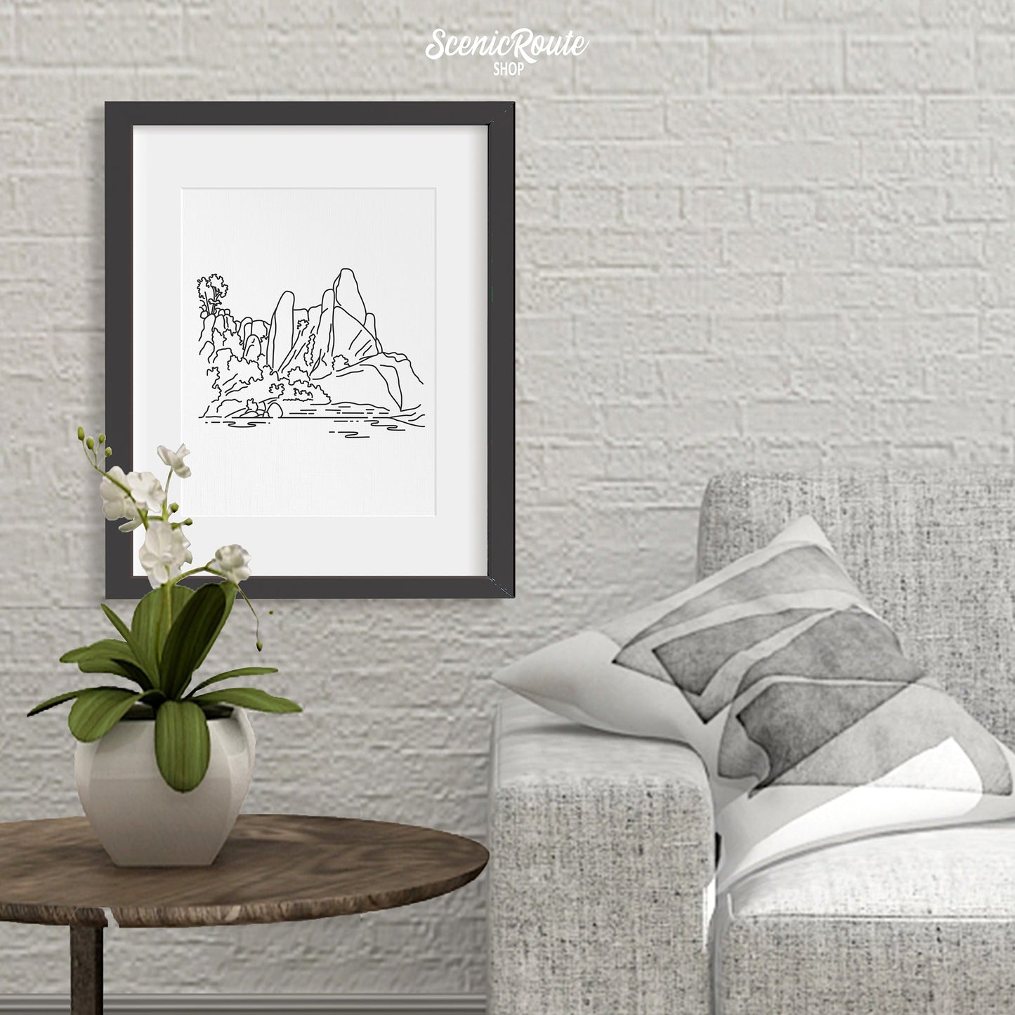 A framed line art drawing of Pinnacles National Park above a side table with an orchid