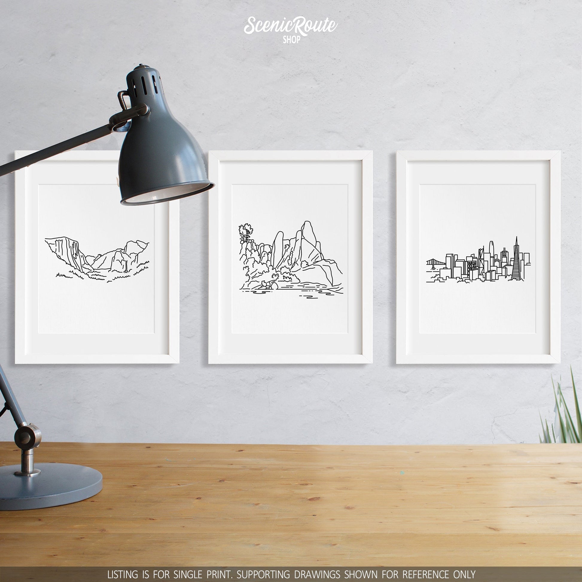 A group of three framed drawings on a wall above a desk with a lamp. The line art drawings include Yosemite National Park, Pinnacles National Park, and the San Francisco Skyline