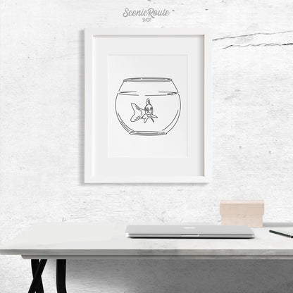 A framed line art drawing of a Goldfish above a desk with a laptop