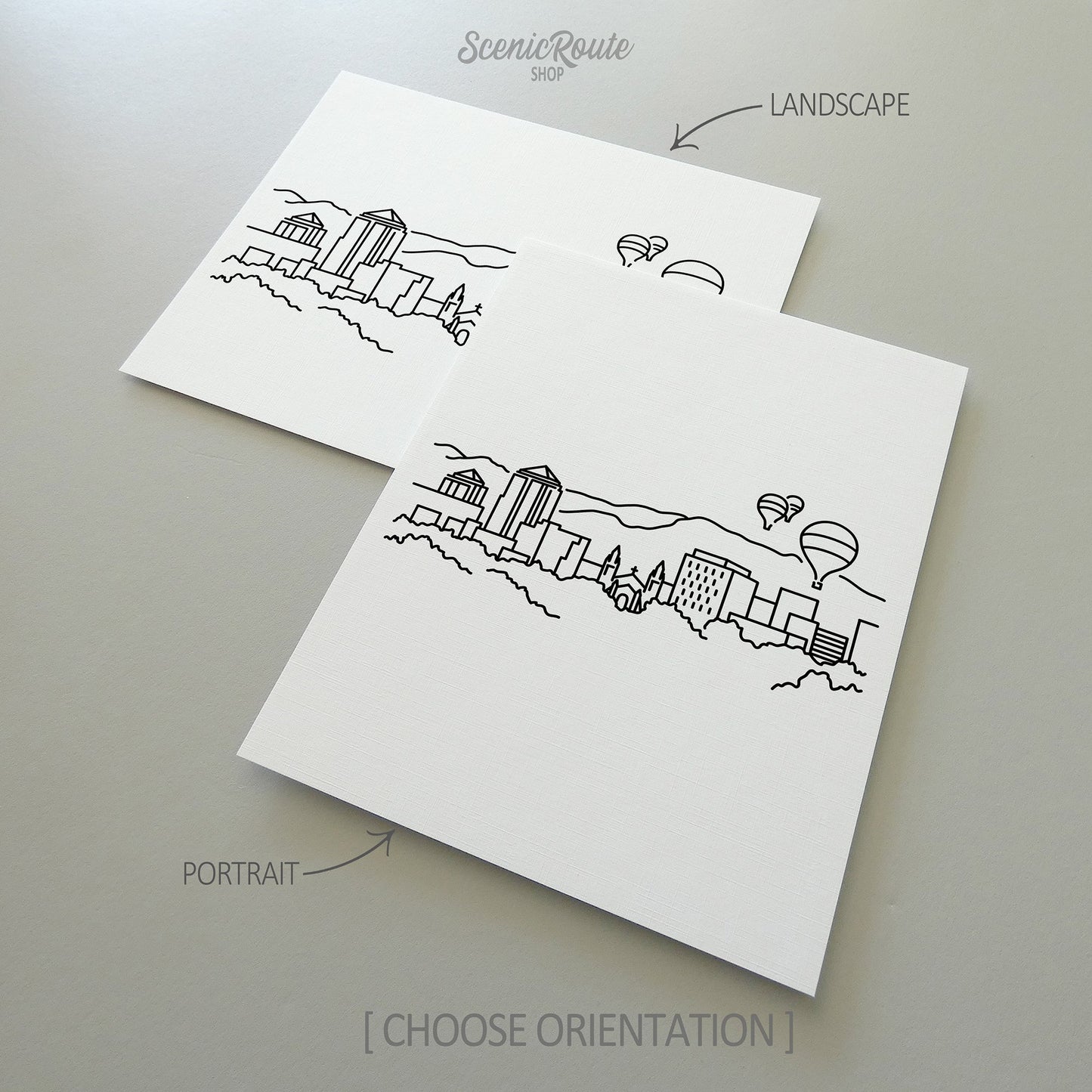 Two line art drawings of the Albuquerque Skyline on white linen paper with a gray background.  The pieces are shown in portrait and landscape orientation for the available art print options.