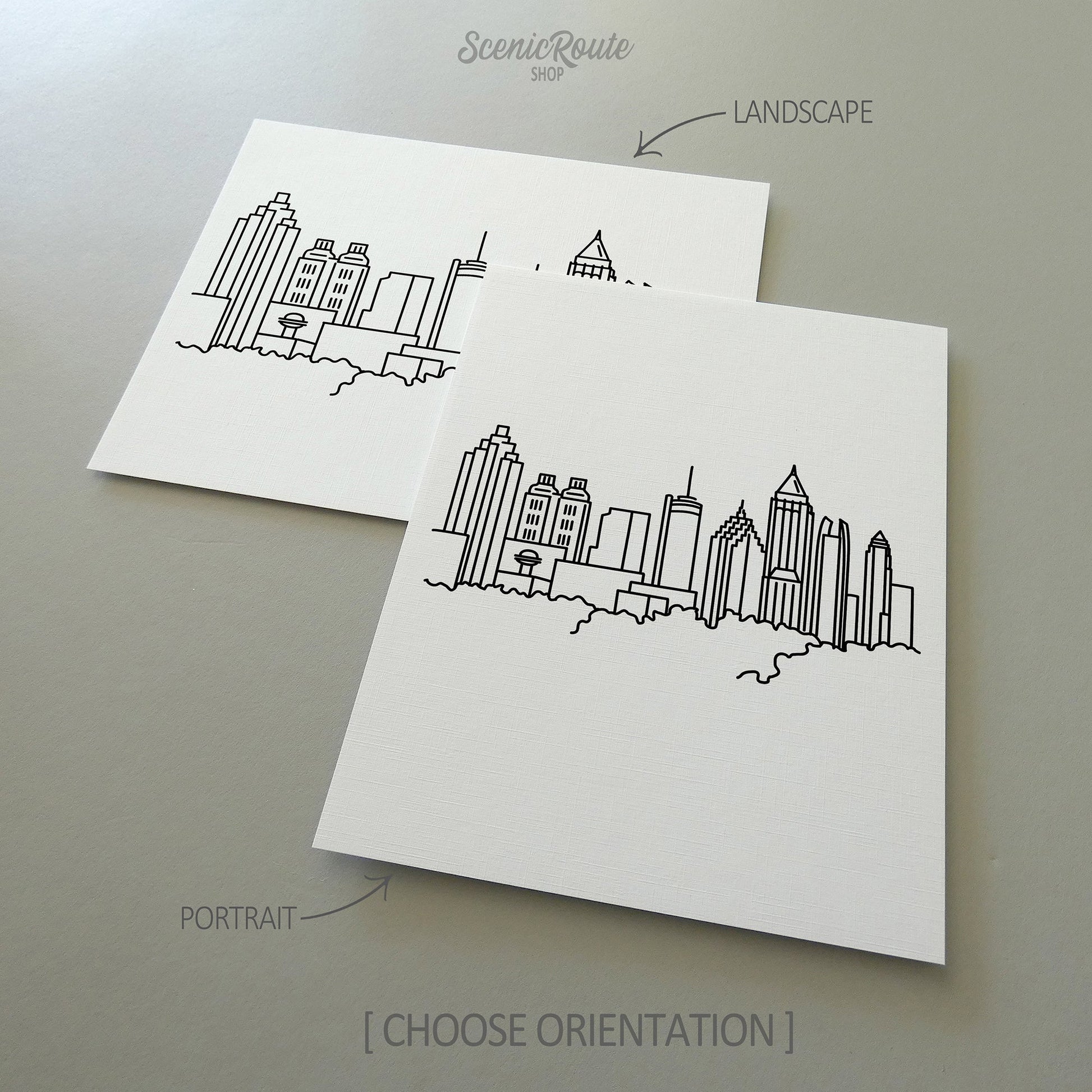 Two line art drawings of the Atlanta Skyline on white linen paper with a gray background.  The pieces are shown in portrait and landscape orientation for the available art print options.