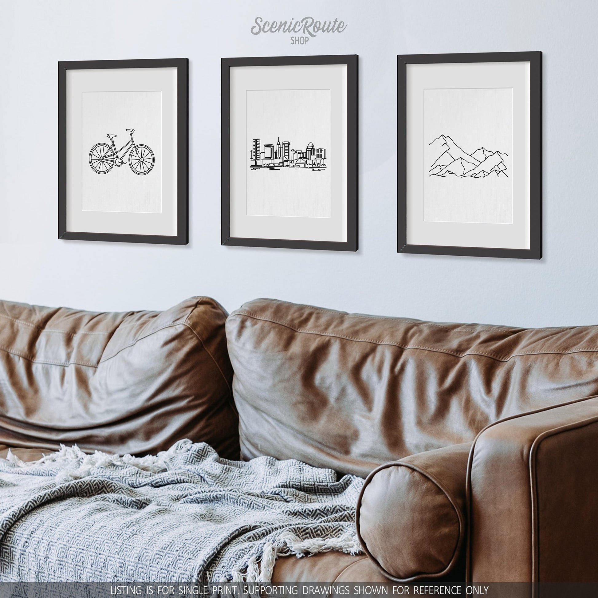 A group of three framed drawings on a wall above a leather couch. The line art drawings include a Bicycle, Baltimore Skyline, and a Mountain Range
