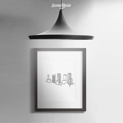 A framed line art drawing of the Birmingham Skyline hanging on a wall with a pendant light above it
