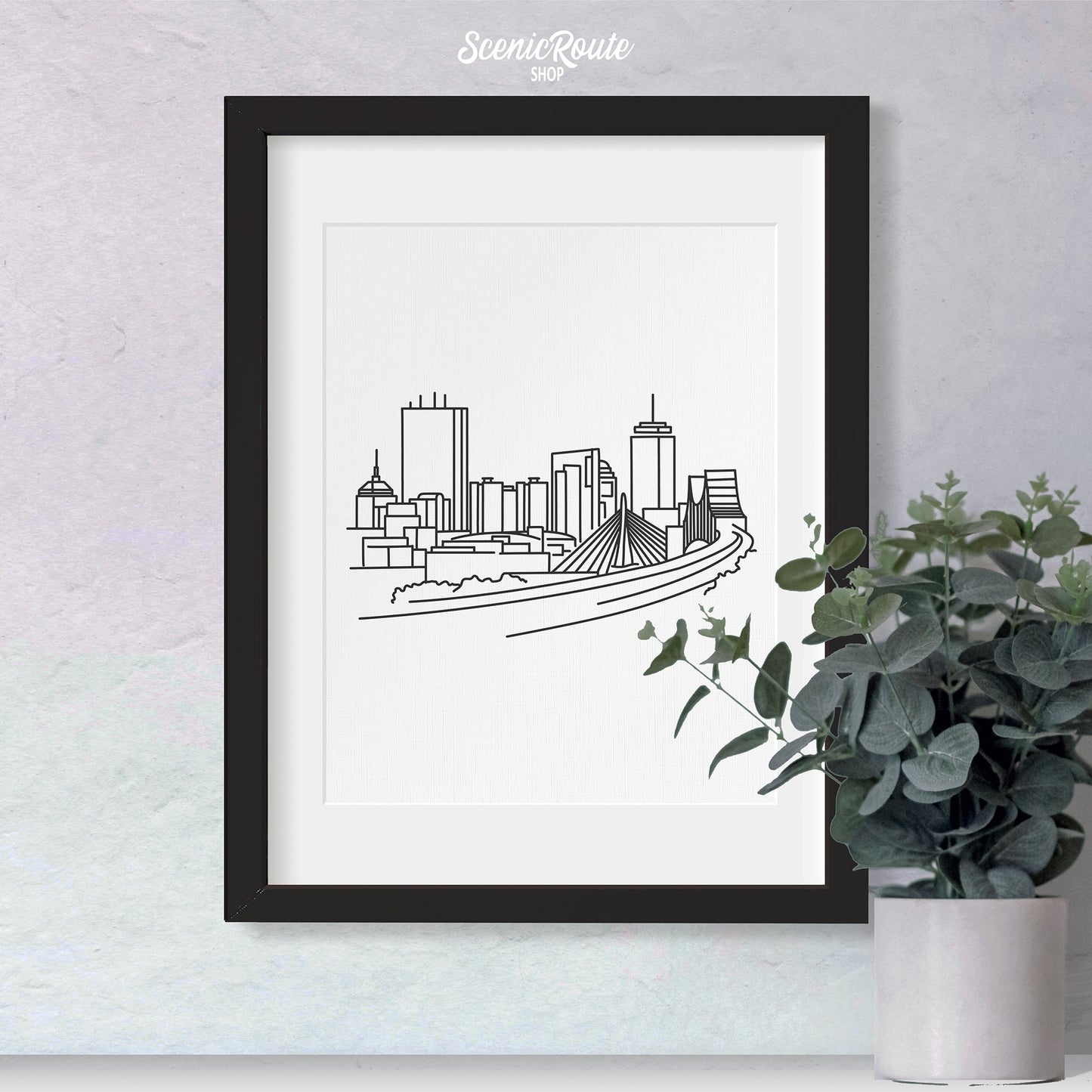 A framed line art drawing of the Boston Skyline with a potted plant
