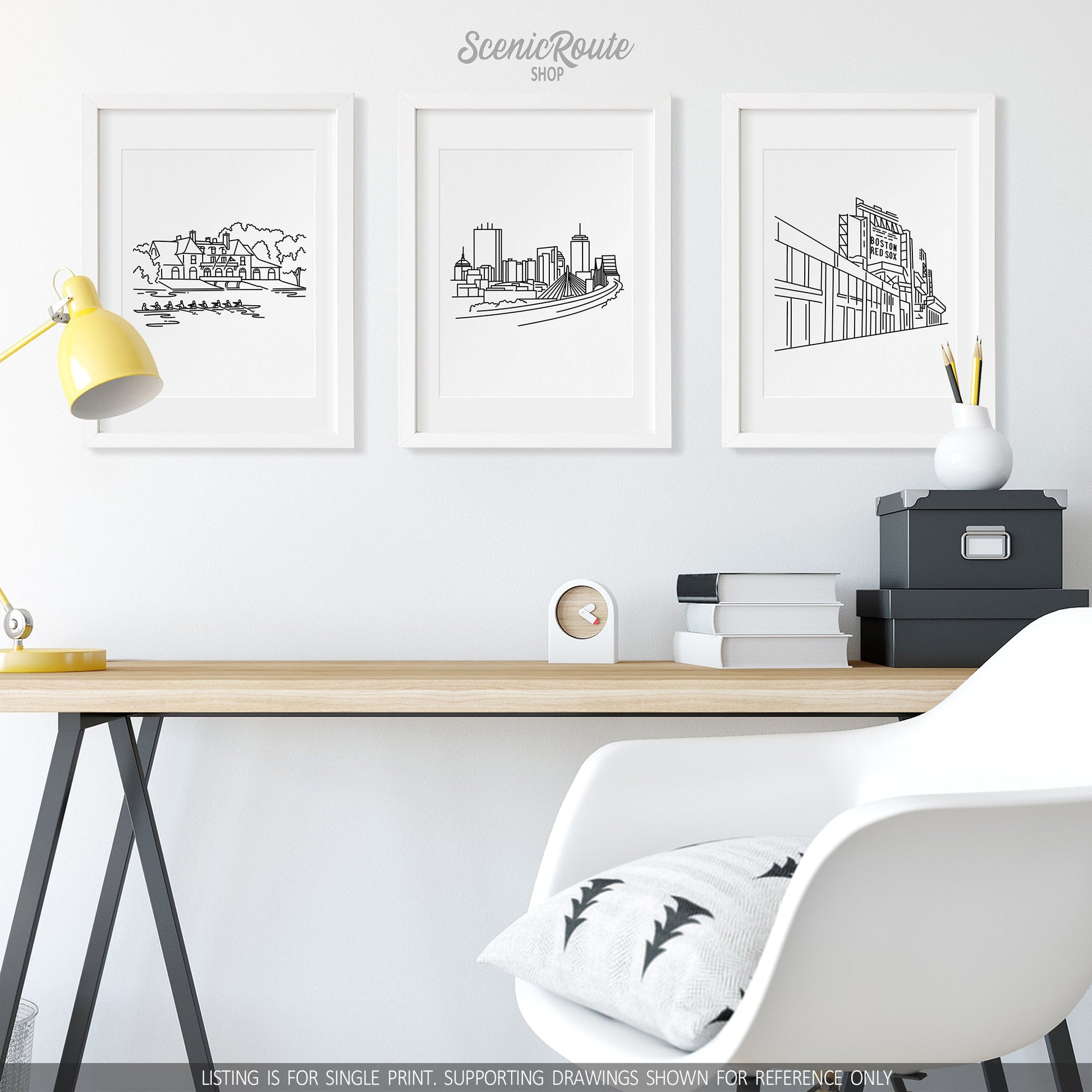 A group of three framed drawings on a wall above a desk. The line art drawings include the Harvard Boathouse, Boston Skyline, and Fenway Park
