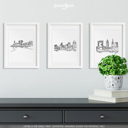 A group of three framed drawings on a wall above a dresser with books and a plant. The line art drawings include the Columbus Skyline, Cincinnati Skyline, and Cleveland Skyline