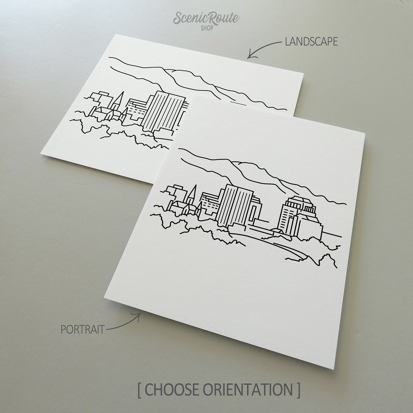 Two line art drawings of the Colorado Springs Skyline on white linen paper with a gray background.  The pieces are shown in portrait and landscape orientation for the available art print options.