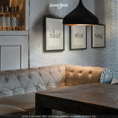 A group of three framed drawings on a brick wall above a leather couch with a hanging pendant light. The line art drawings include the San Antonio Skyline, Dallas Skyline, and Austin Skyline