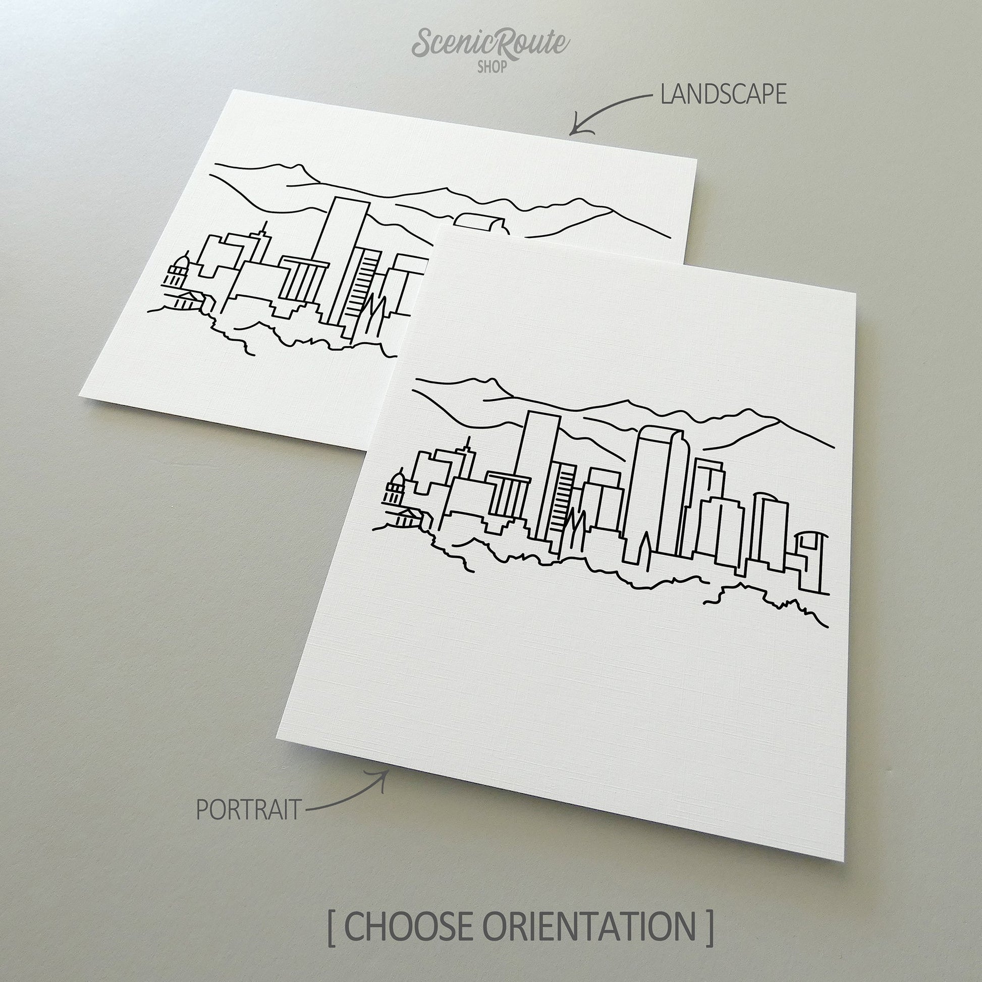 Two line art drawings of the Denver Skyline on white linen paper with a gray background.  The pieces are shown in portrait and landscape orientation for the available art print options.