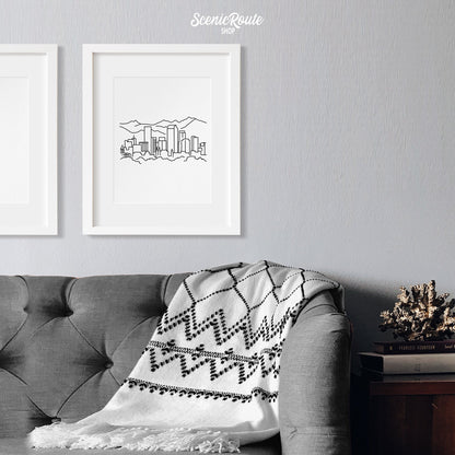 A framed line art drawing of the Denver Skyline hanging above a couch with a blanket