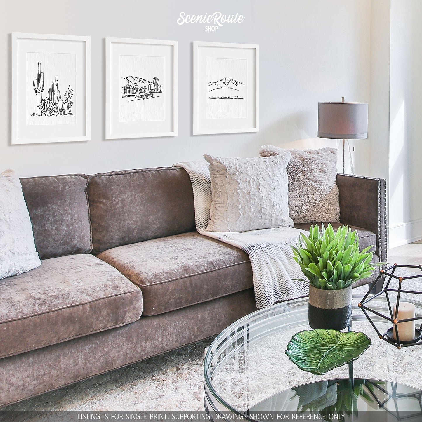 A group of three framed drawings on a white wall hanging above a couch with pillows and a blanket. The line art drawings include a Cactus Garden, Flagstaff Skyline, and Humphreys Peak