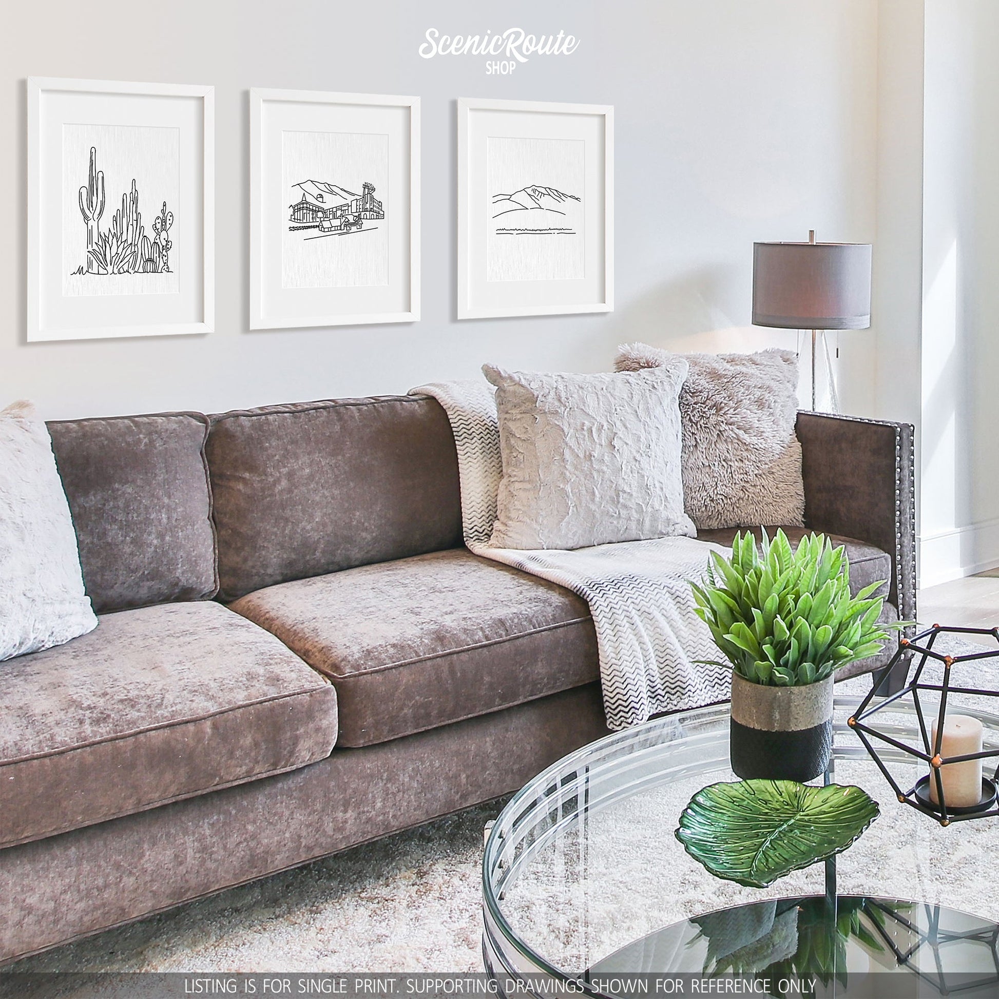 A group of three framed drawings on a white wall hanging above a couch with pillows and a blanket. The line art drawings include a Cactus Garden, Flagstaff Skyline, and Humphreys Peak