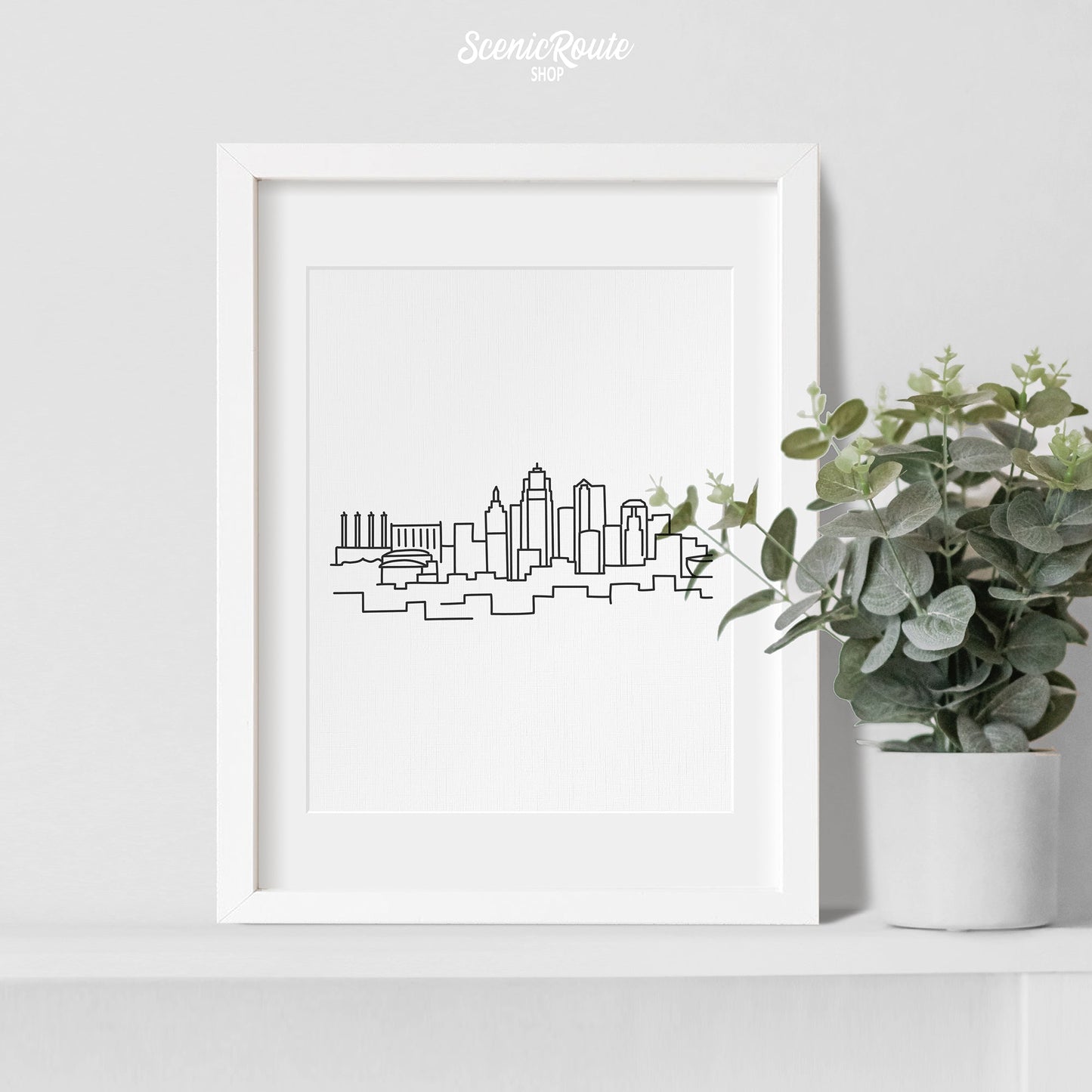 A framed line art drawing of the Kansas City Skyline with a potted plant