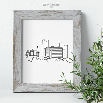 A framed line art drawing of the Lexington Skyline with greenery