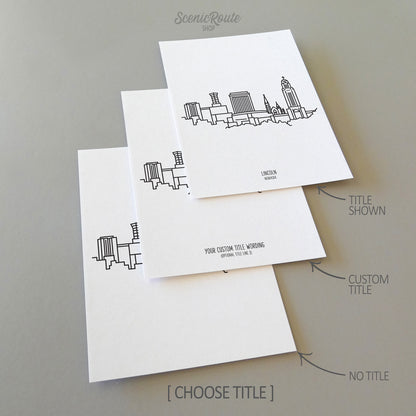 Three line art drawings of the Lincoln Nebraska Skyline on white linen paper with a gray background. The pieces are shown with title options that can be chosen and personalized.