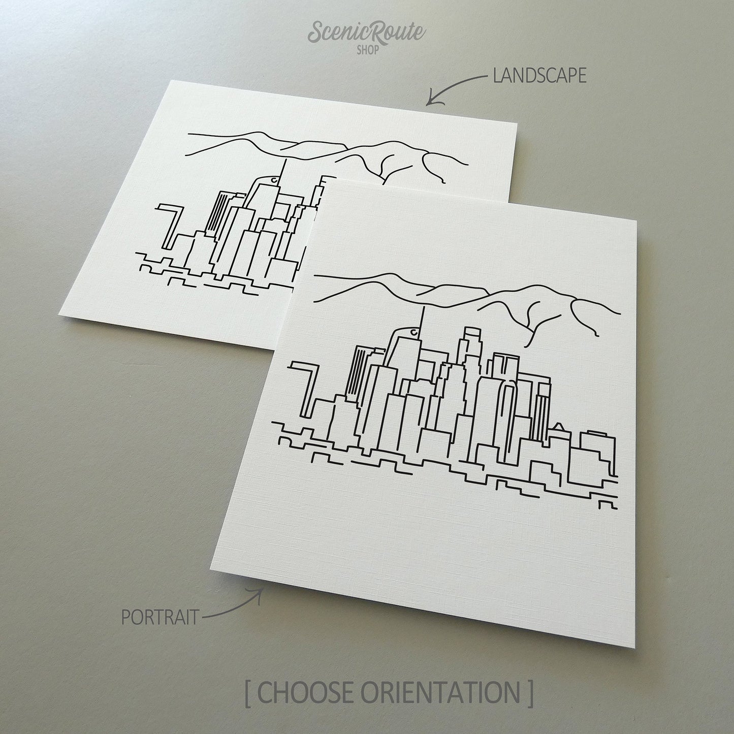 Two line art drawings of the Los Angeles Skyline on white linen paper with a gray background.  The pieces are shown in portrait and landscape orientation for the available art print options.