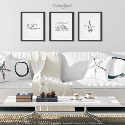 A group of three framed drawings on a white wall hanging above a couch with pillows and a blanket. The line art drawings include Waves, Los Angeles Skyline, and Sailing