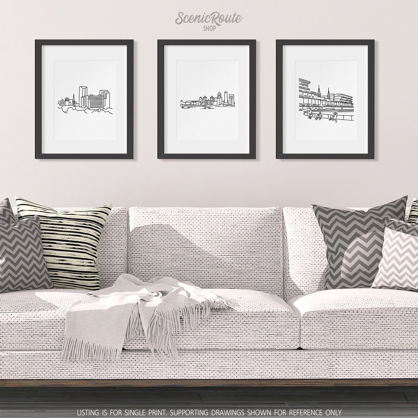A group of three framed drawings on a white wall hanging above a couch with pillows and a blanket. The line art drawings include the Lexington Skyline, Louisville Skyline, and Churchill Downs