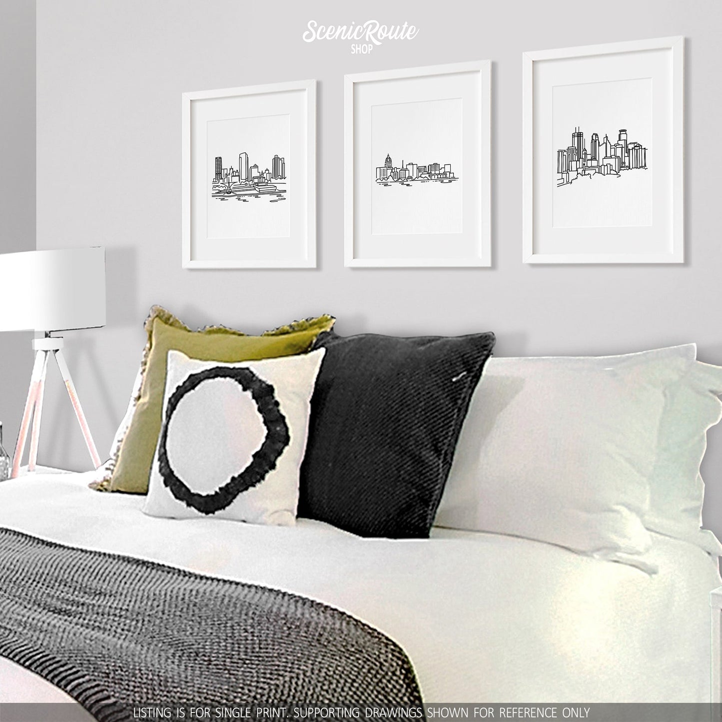 A group of three framed drawings on a white wall above a bed. The line art drawings include the Milwaukee Skyline, Madison Skyline, and Minneapolis Skyline