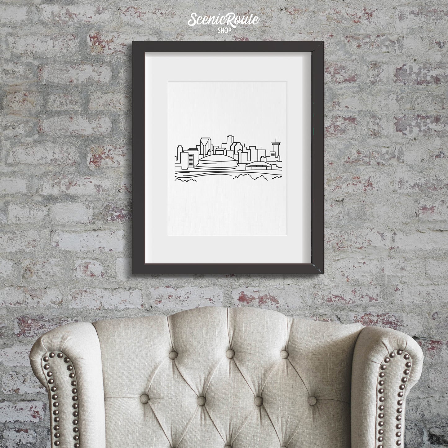 A framed line art drawing of the New Orleans Skyline hanging on a brick wall above a chair