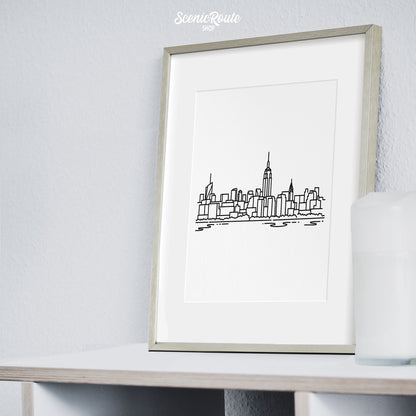 A framed line art drawing of the New York City Skyline sitting on a bookcase