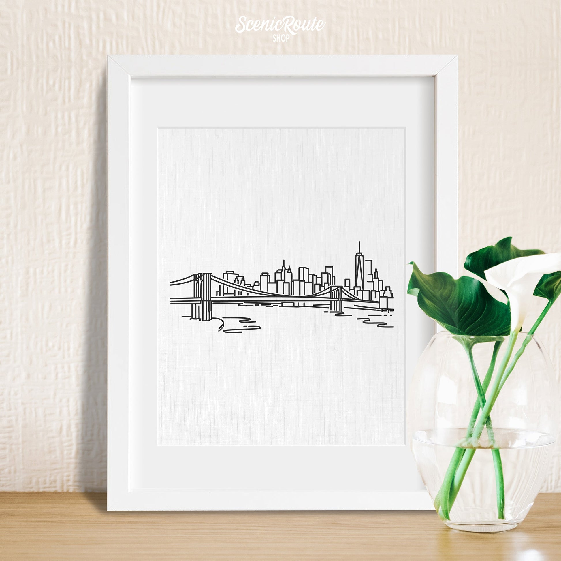 A framed line art drawing of the New York City Skyline with a vase