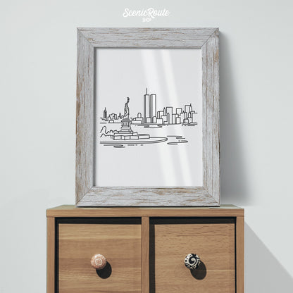 A framed line art drawing of the New York City Skyline sitting on a small cabinet
