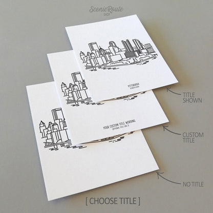 Three line art drawings of the Pittsburgh Pennsylvania Skyline on white linen paper with a gray background. The pieces are shown with title options that can be chosen and personalized.