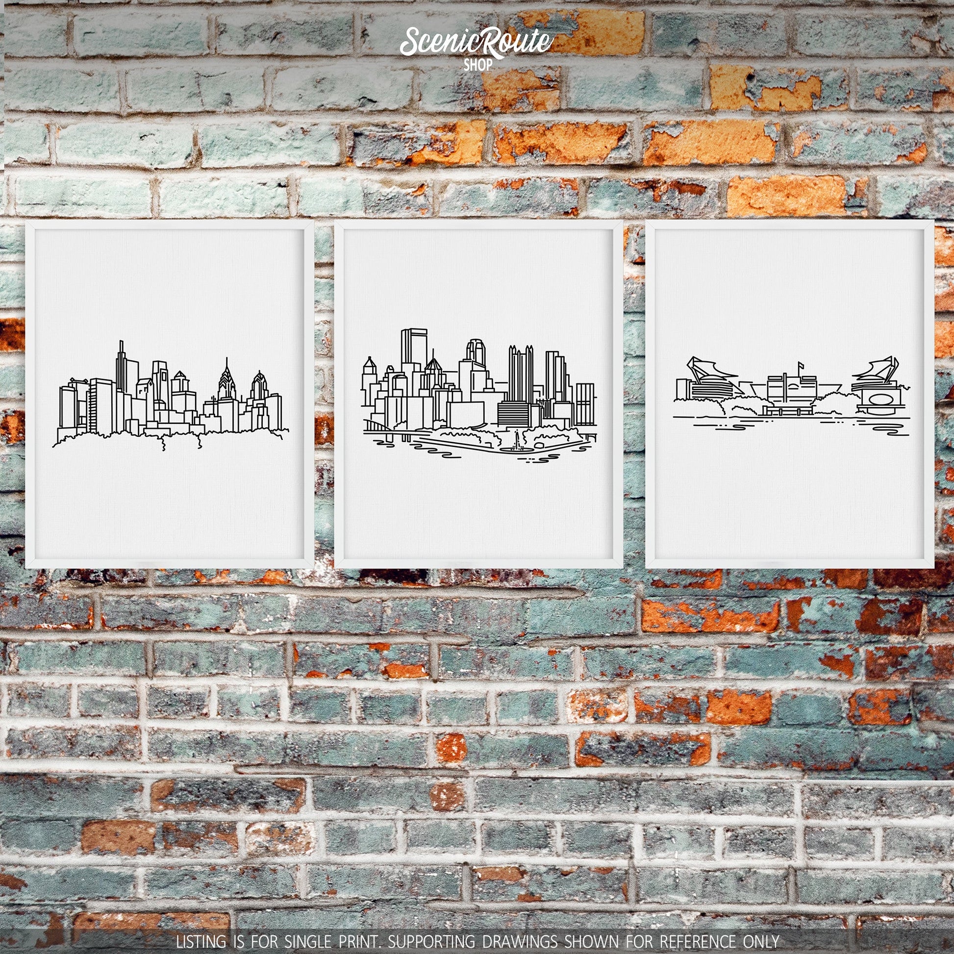 A group of three framed drawings on a brick wall. The line art drawings include the Philadelphia Skyline, Pittsburgh Skyline, and Pittsburgh Steelers Stadium