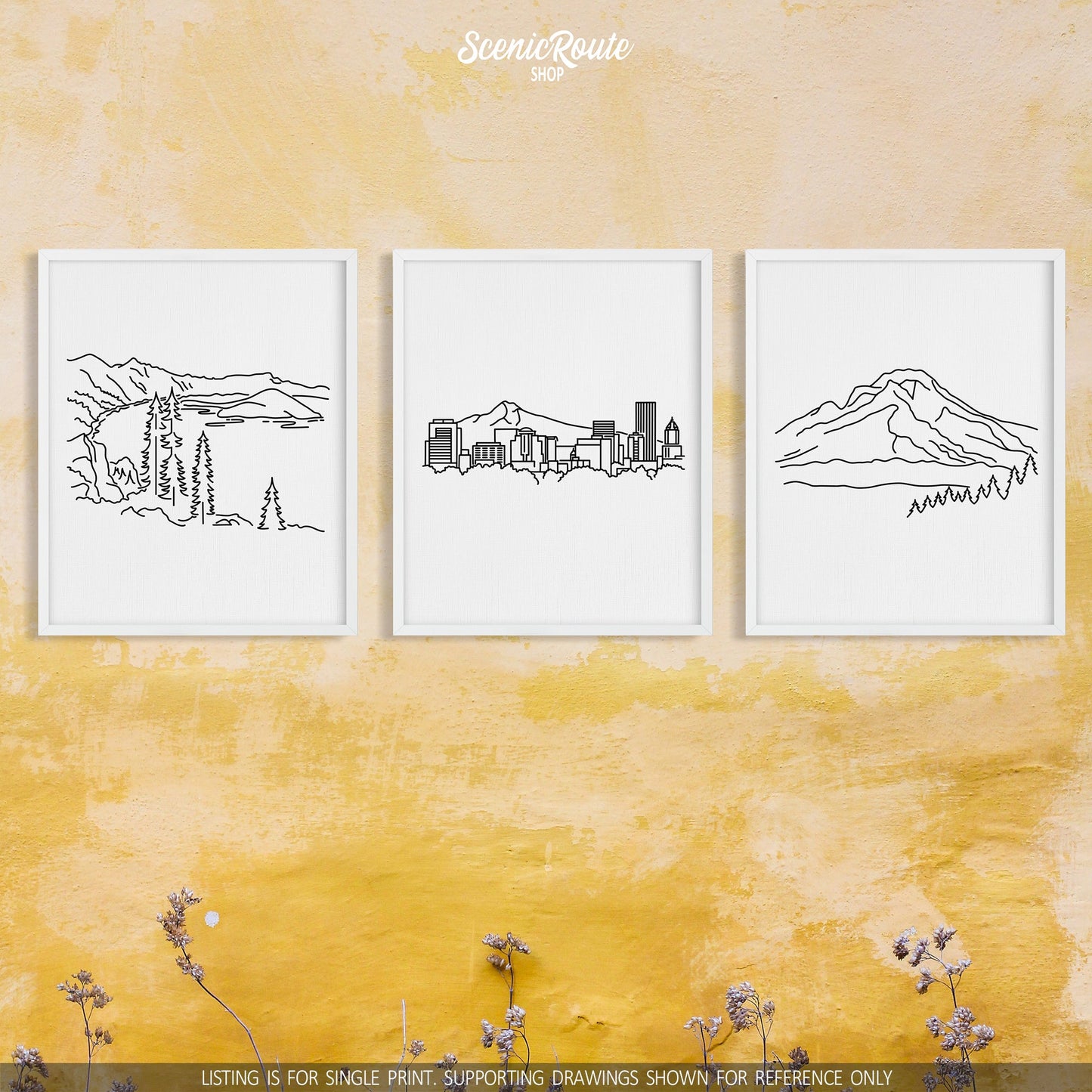 A group of three framed drawings on a yellow wall. The line art drawings include Crater Lake National Park, the Portland Skyline, and Mount Hood