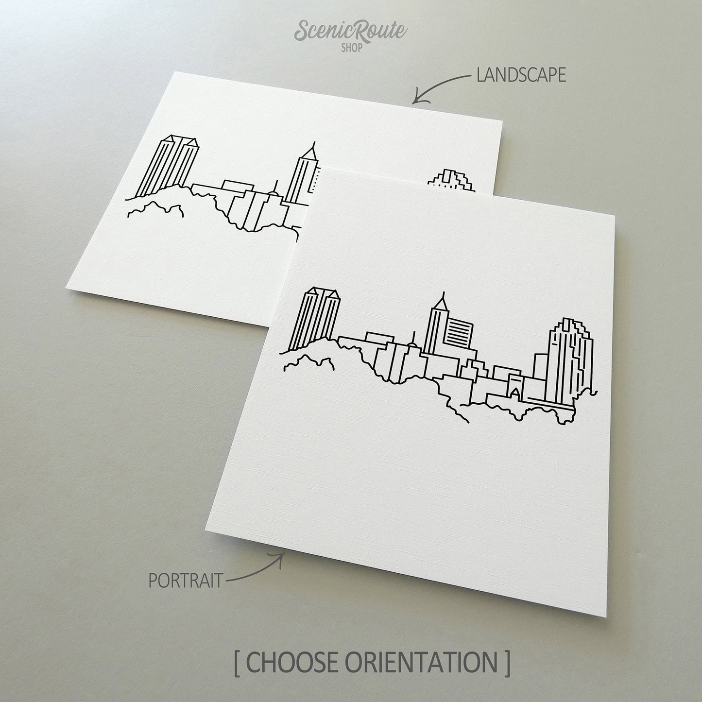 Two line art drawings of the Raleigh Skyline on white linen paper with a gray background.  The pieces are shown in portrait and landscape orientation for the available art print options.