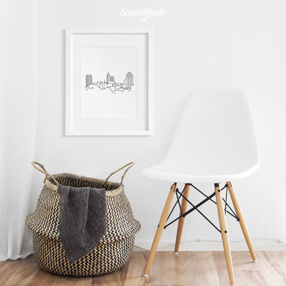 A framed line art drawing of the Raleigh Skyline above a basket and chair