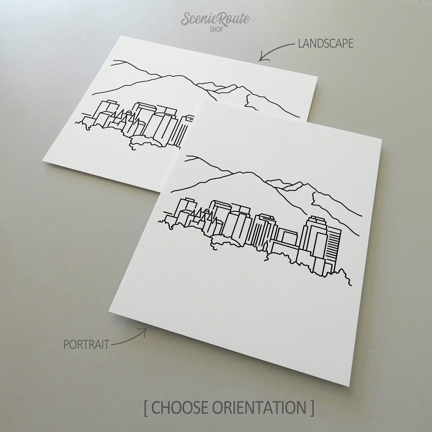 Two line art drawings of the Salt Lake City Skyline on white linen paper with a gray background.  The pieces are shown in portrait and landscape orientation for the available art print options.