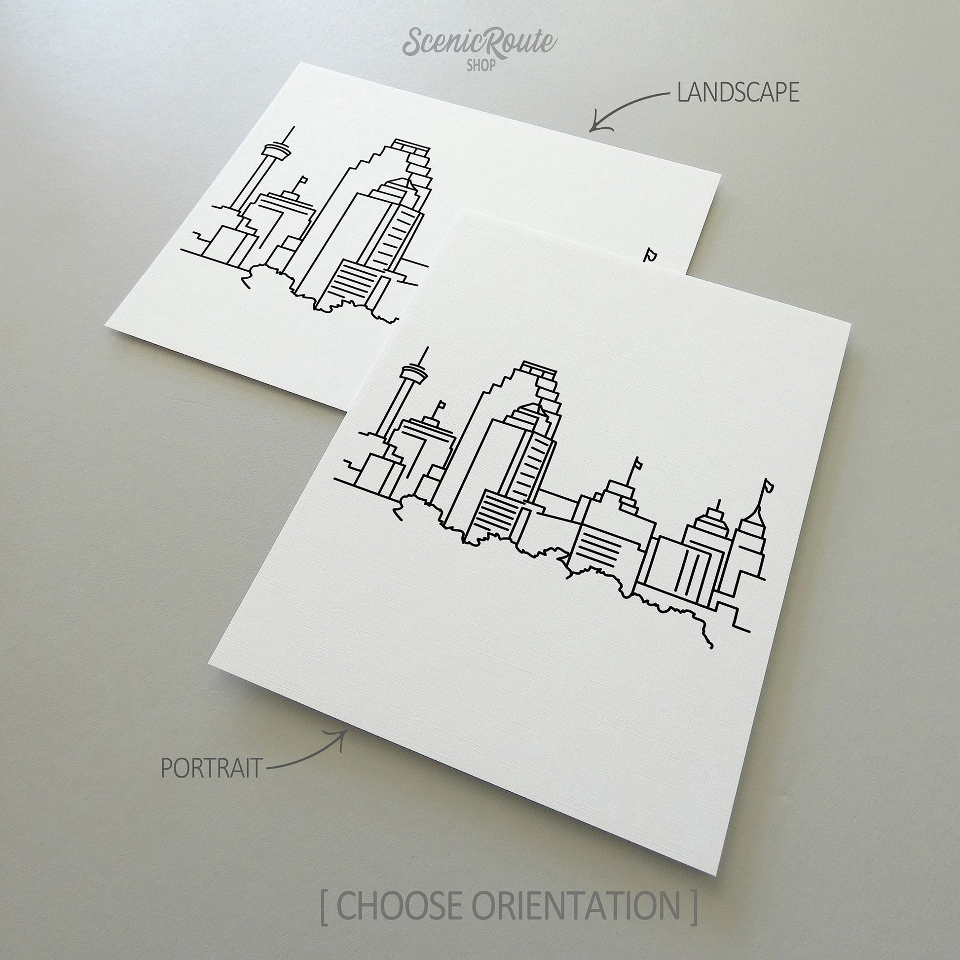 Two line art drawings of the San Antonio Skyline on white linen paper with a gray background.  The pieces are shown in portrait and landscape orientation for the available art print options.