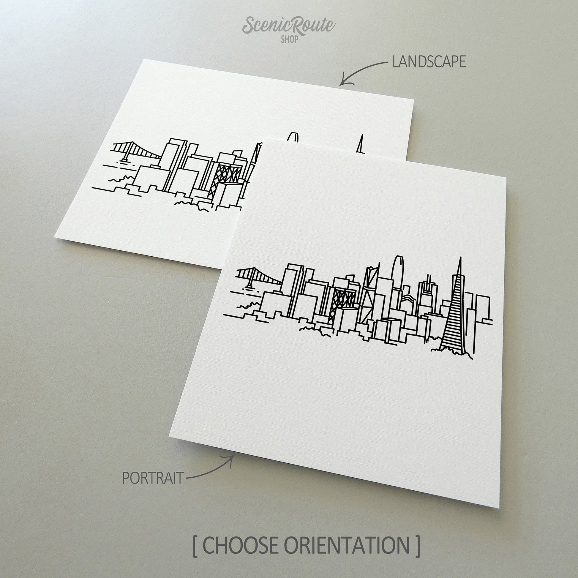 Two line art drawings of the San Francisco Skyline on white linen paper with a gray background.  The pieces are shown in portrait and landscape orientation for the available art print options.