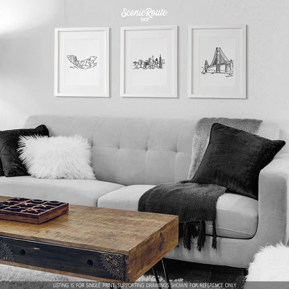 A group of three framed drawings on a white wall hanging above a couch with pillows and a blanket. The line art drawings include Yosemite National Park, San Francisco Skyline, and the Golden Gate Bridge