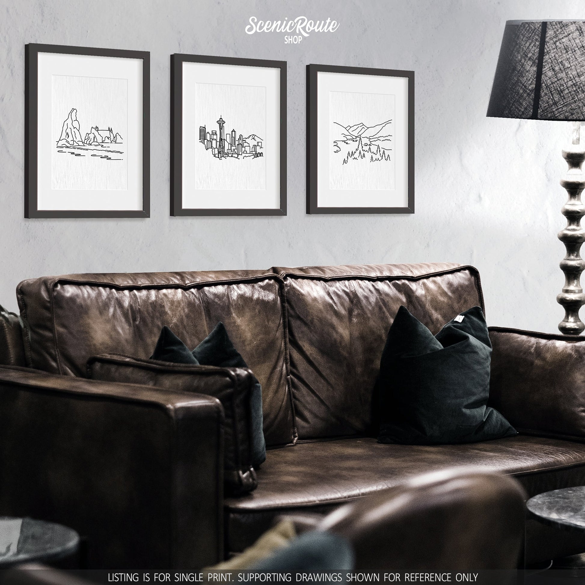 A group of three framed drawings on a wall above a couch. The line art drawings include Olympic National Park, Seattle Skyline, and North Cascades National Park