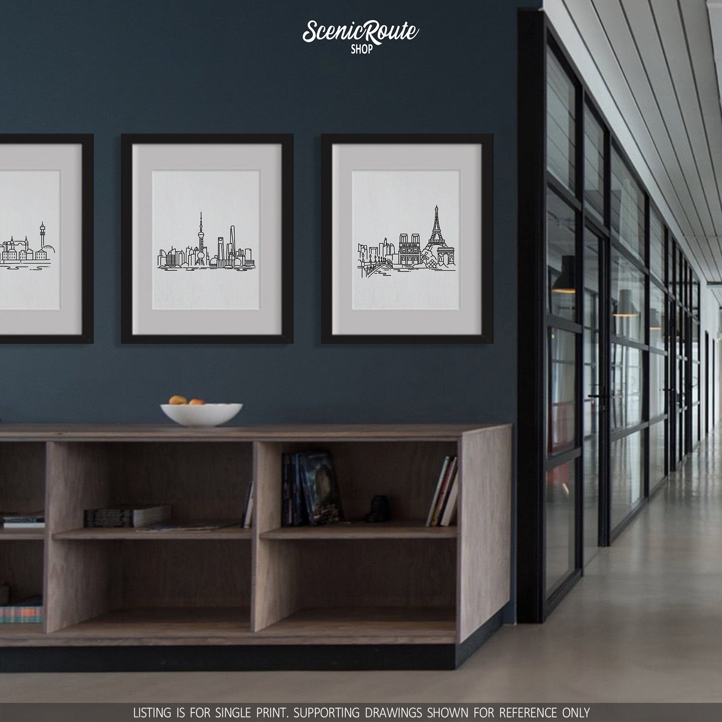 A group of three framed drawings hanging on the wall above cabinets in a modern office. The line art drawings include the Stockholm Skyline, Shanghai Skyline, and Paris Skyline
