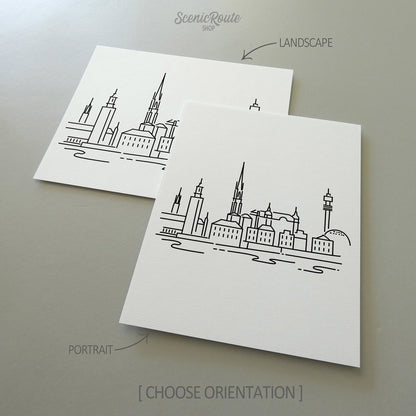 Two line art drawings of the Stockholm Skyline on white linen paper with a gray background.  The pieces are shown in portrait and landscape orientation for the available art print options.