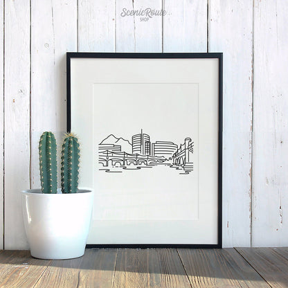 A framed line art drawing of the Tempe Skyline with a potted cactus